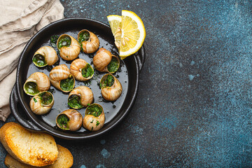 Escargots de Bourgogne Snails with Garlic Butter and Parsley in black cast iron pan with Lemon and...