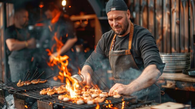 A professional chef is seen flipping seafood on a grill amongst robust flames at an outdoor eatery