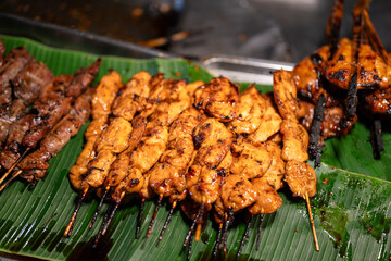 Group of grilled BBQ chicken meat in wooden skewers, placed on banana leaf at local market. Street food object photo, close-up.