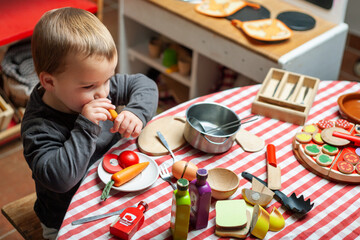 Toddler plays at eating food in playroom. Wooden toys, symbolic play.