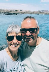 Portrait of  young adult couple,in love and smiling,on holiday in Tenerife,taking a selfie,against a blue-sky and sea background.Couple of tourists in love and enthusiastic taking a selfie,in Tenerife
