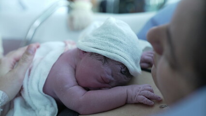 Close-up of Newborn baby after birth, first seconds of life, nurse's hand putting warm clothes,...