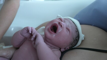 Crying newborn baby right after birth, firsts breath of an infant first seconds of life during childbirth