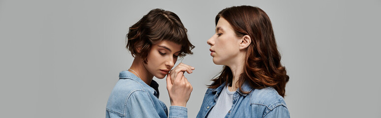 Two young women in denim attire pose against a grey background, showcasing their stylish fashion choices.