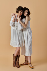 Two young women in white summer dresses stand close together on a beige background. Lesbian couple