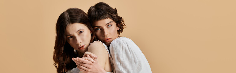 Two young women in white summer dresses pose together against a beige background.