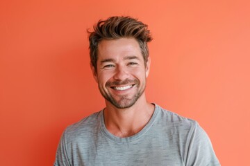 Fototapeta premium Portrait of a glad man in his 30s smiling at the camera isolated on pastel orange background