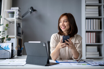 A woman is sitting at a desk with a laptop and a cell phone