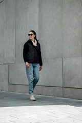 Obraz premium Walking woman with black jacket, blue jeans and sunglasses