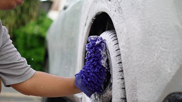 man holding sponge, washing car wheel with foam. Cleaning of modern rims of luxury  car at self car wash service outdoors
