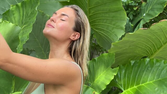 Woman using mist spray for moisturizing her face in front of tropical leaves