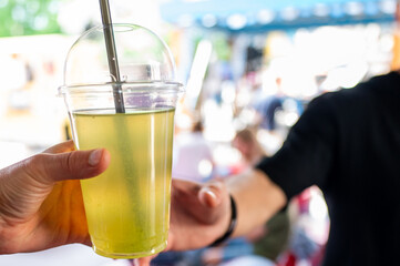 Close-up of a hand holding a transparent cup with a yellow drink and straw against an out-of-focus background