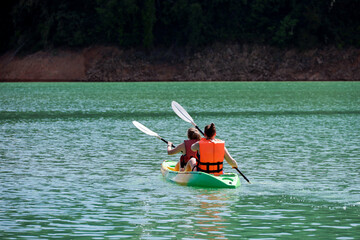 Two girls in life vests riding kayak on mountain lake, summer leisure