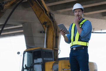 worker using pc. civil engineer order job by radio communication with back hole on background in site construction.