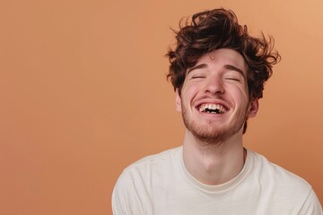 Obraz premium Portrait of a glad man in his 20s laughing while standing against pastel brown background