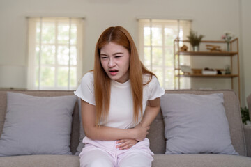 Young Woman Experiencing Stomach Pain While Sitting on a Couch in a Bright Living Room