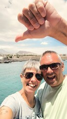 Portrait of young adult couple,in love and happy, taking a selfie,he makes the ok sign with his fingers. Happy tourist couple,taking a selfie,he confirms the perfect vacation.Perfect couple selfie.