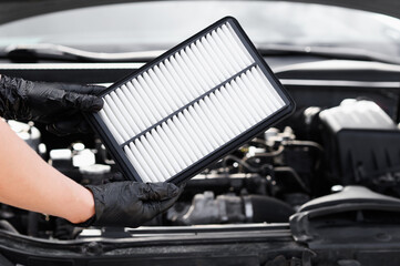 Person holds air filter in front of car engine, checks and replaces it to ensure optimal performance of car. Replacing air filter in a car. Car maintenance and repair.
