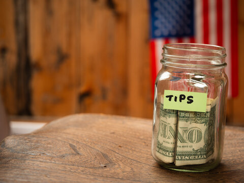 Tip jar with dollars and American flag background c