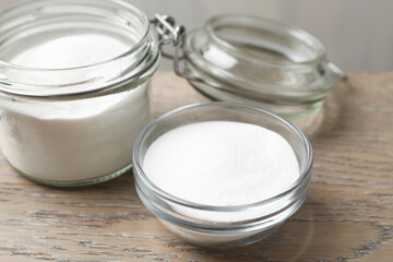 Baking soda in bowl and glass jar on wooden table, closeup