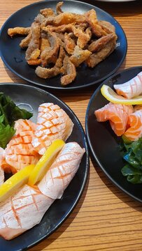 Salmon Belly Shasimi and fried Salmon skin, a Japanese popular food with lime on a black plate.