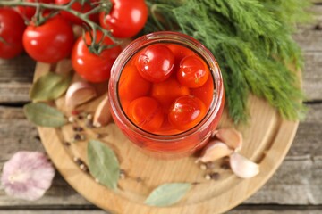 Tasty pickled tomatoes in jar, fresh vegetables and spices on wooden table, top view