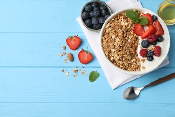 Tasty granola with berries and yogurt in bowl on light blue wooden table, flat lay. Space for text
