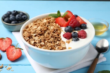 Tasty granola with berries and yogurt in bowl on light blue wooden table, closeup