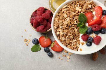 Tasty granola with berries and yogurt in bowl on grey textured table, flat lay. Space for text