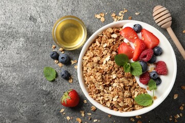 Tasty granola with berries, yogurt and honey on grey textured table, flat lay. Space for text