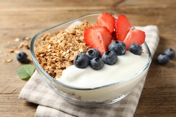 Tasty granola with berries and yogurt in bowl on wooden table, closeup