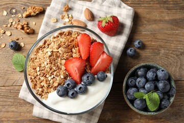 Tasty granola with berries and yogurt in bowl on wooden table, flat lay