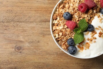 Tasty granola with berries and yogurt on wooden table, top view. Space for text