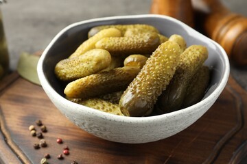 Pickled cucumbers in bowl and peppercorns on wooden board, closeup