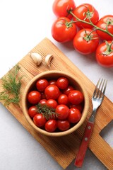 Tasty pickled tomatoes in bowl, fresh vegetables, dill, garlic and fork on white table, top view