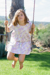 beautiful little girl in a colorful dress sitting on a swing on a green meadow