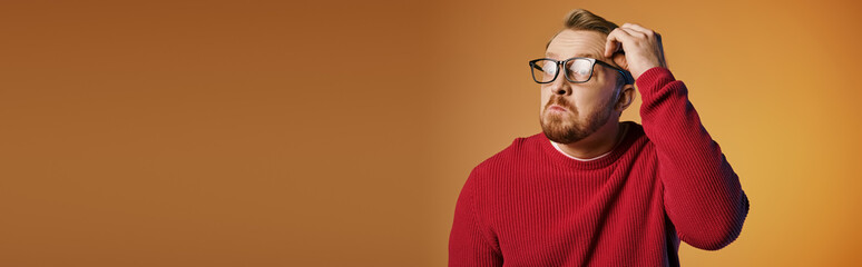 A man in a red sweater holds his head in deep thought.