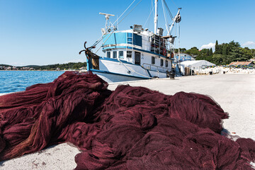 Bright red fishing net on concrete embankment with a fishing boat on the background. Croatia