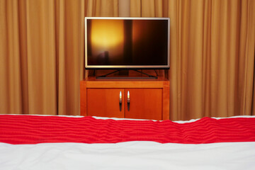 A flat screen television is on a wooden stand in front of a curtain reflecting room ambient light....