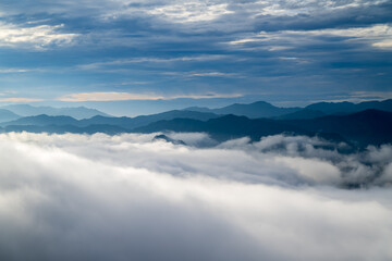 The sunlight makes the sea of clouds change unpredictably, like stormy waves. View of the mountains surrounding Emerald Reservoir. Xindian District, Taiwan.