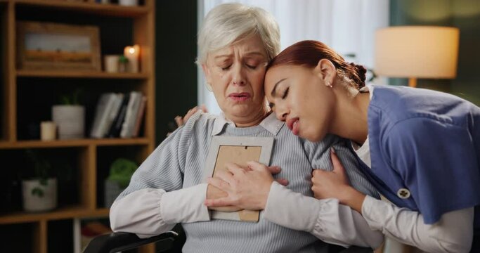 Senior, woman and nurse with photo for support with grief, memory and mourning in home with hugging lost love. Elderly, person or caregiver with picture frame in wheelchair for remember or compassion