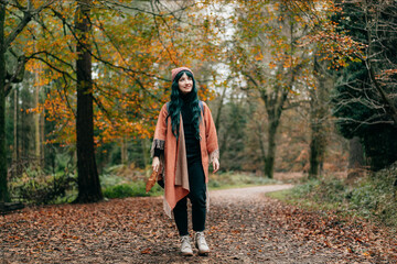 Hipster woman wrapped in Shawl Poncho with backpack enjoying autumn walk in forest with fall leaves. Feeling harmony, reunion with nature. Relaxing, personal fulfillment. Local travel lifestyle.