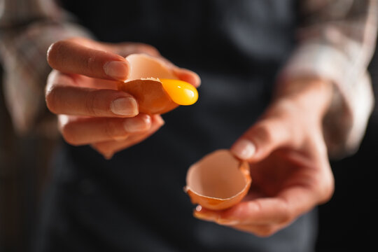 Female baker's hands cracking an egg with yolk dripping out, preparing for baking.