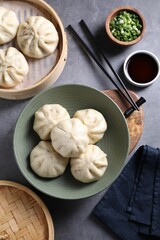 Delicious bao buns (baozi), chopsticks, soy sauce and green onion on grey table, flat lay