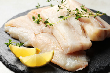 Pieces of raw cod fish and lemon on table, closeup
