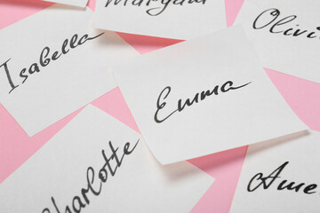 Paper stickers with different names on pink background, closeup. Choosing baby's name