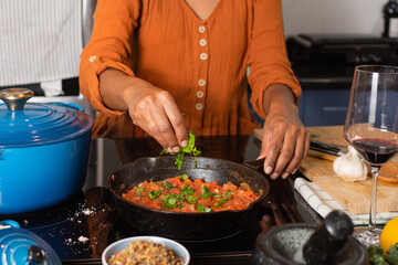 Close-up of a woman's hands standing by the stove, adding chopped basil to fresh tomato sauce