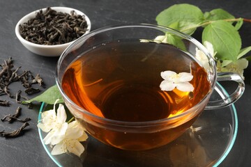 Aromatic jasmine tea in glass cup, flowers and dry leaves on grey table, closeup