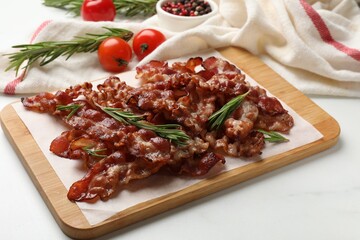 Slices of tasty fried bacon with rosemary on white table