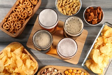 Glasses with different types of beer and snacks on grey wooden table, flat lay